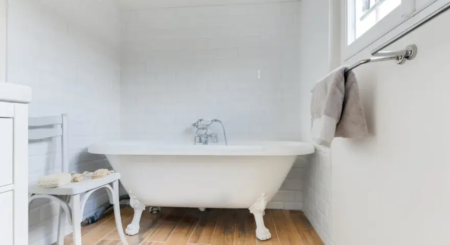 Baignoire îlot blanche sur pieds, robinetterie argentée. La hauteur baignoire est standard, avec un petit tabouret à côté.