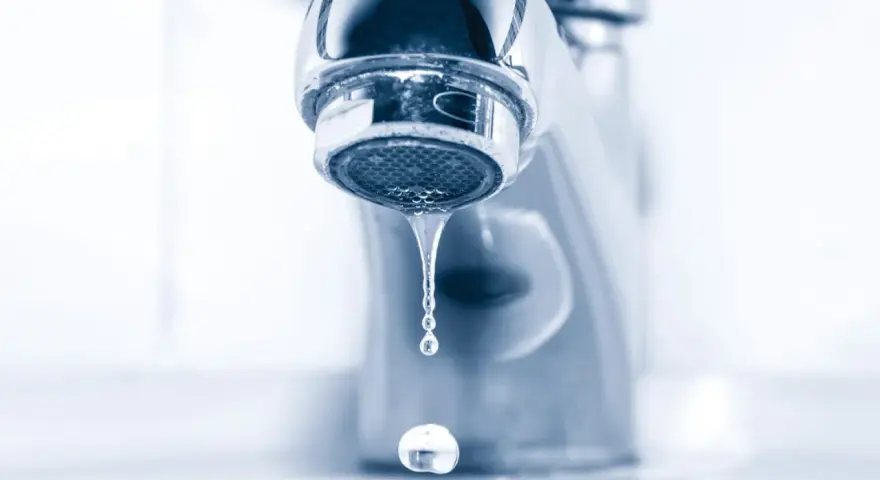 Gouttelettes d'eau tombant d'un robinet de salle de bain qui fuit. Un petit désagrément qui coûte cher.