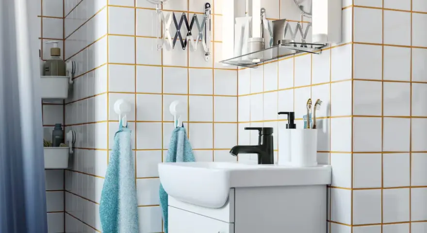 Salle de bain moderne avec carrelage blanc joint gris, lavabo, robinetterie noire et accessoires pratiques.