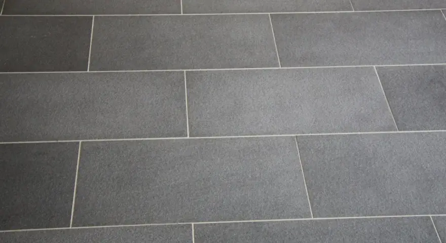 Détail d'un sol en carrelage gris anthracite, avec un joint carrelage couleur crème qui souligne la pose rectiligne.