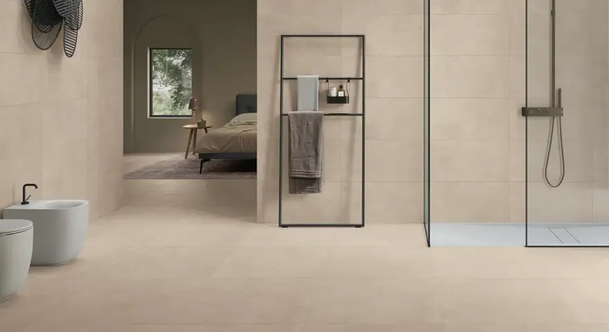 Salle de bain moderne avec bidet, douche et lit visible au loin, le tout revêtu de grès cérame émaillé.
