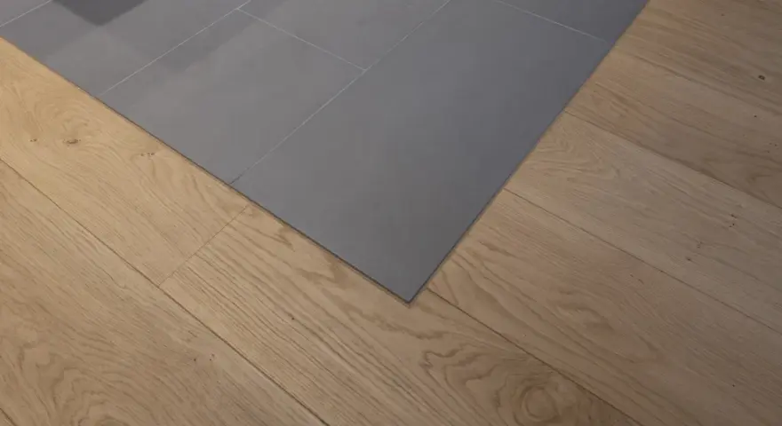 Un coin de sol où le carrelage gris imitation parquet rencontre un parquet en bois naturel. La couleur du joint du carrelage est discrète.
