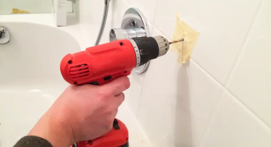 Main tenant utilise une perceuse pour percer le carrelage de la salle de bain, afin d'y fixer un accessoire.