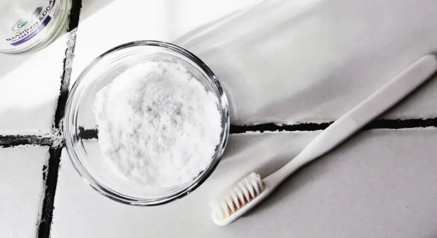 Bicarbonate de soude dans un bol et une brosse à dents sur un carrelage.
