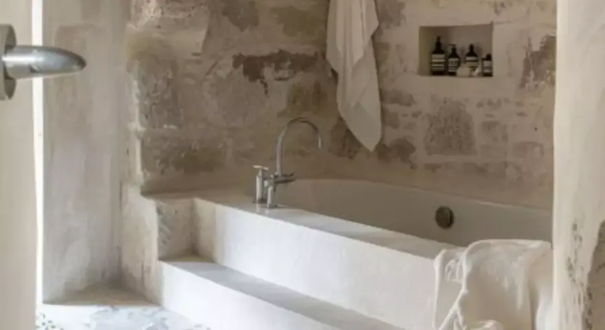 Une **salle de bain méditerranéenne** avec baignoire en pierre brute, robinetterie moderne et serviette blanche suspendue. Ambiance zen.
