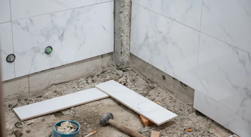 Travaux de pose de faience salle de bain : des carreaux de marbre blanc sont prêts à être installés, avec des outils au sol.