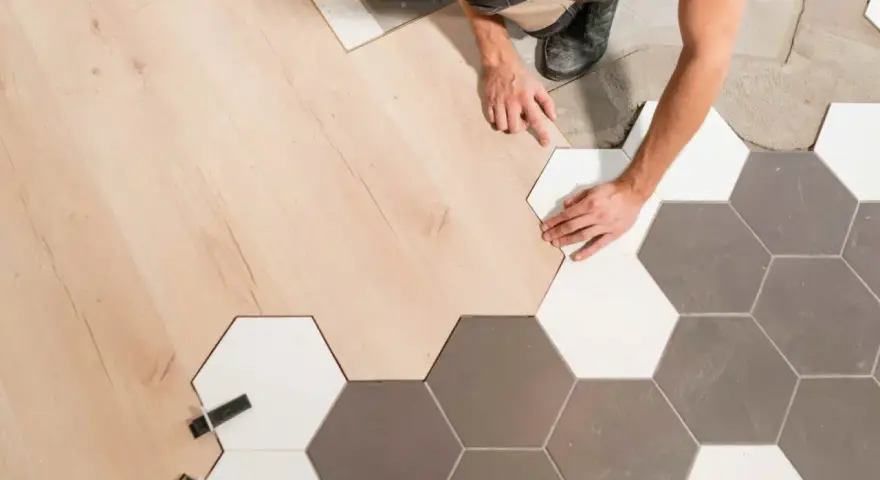 Pose d'un parquet bois clair et de carreaux hexagonaux gris et blancs. La jonction parquet carrelage est en cours de réalisation par un artisan.