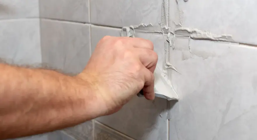 Main d'une personne appliquant du mastic sur les joints d'une salle de bain.