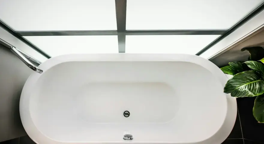 Vue aérienne d'une baignoire blanche moderne, prête à accueillir un bain relaxant. La contenance baignoire est généreuse, sous un puits de lumière.