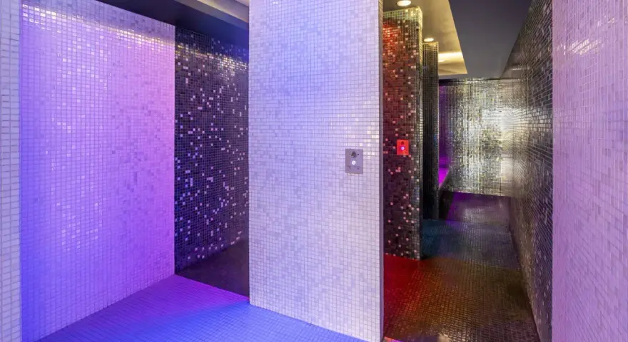 Un espace de détente aux murs recouverts de mosaïques scintillantes, baigné de lumières violettes et bleues. Une invitation à une douche sensorielle immersive.