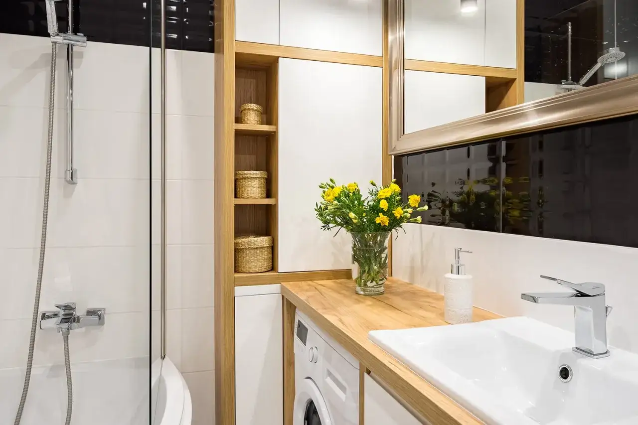 Idée petite salle de bain avec baignoire : douche, lavabo, machine à laver et rangements en bois. Fleurs jaunes pour une touche de couleur.