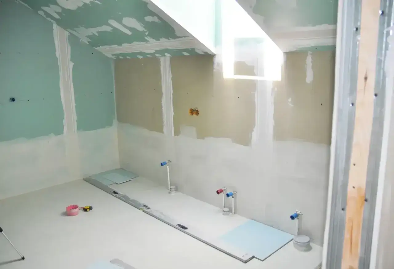 Chantier de salle de bain : murs en plaques de plâtre, tuyauterie apparente, niveau à bulle et outils au sol. Travaux d'isolation salle de bain en cours.