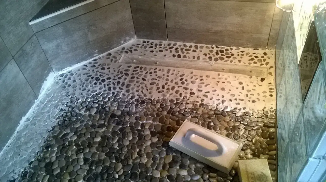 Application d'un joint époxy sur un sol de douche en galets. Un outil blanc est posé sur les galets.