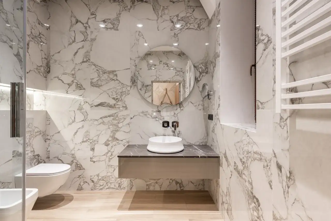Salle de bain moderne au style toilette, avec murs en marbre, lavabo suspendu et miroir rond.