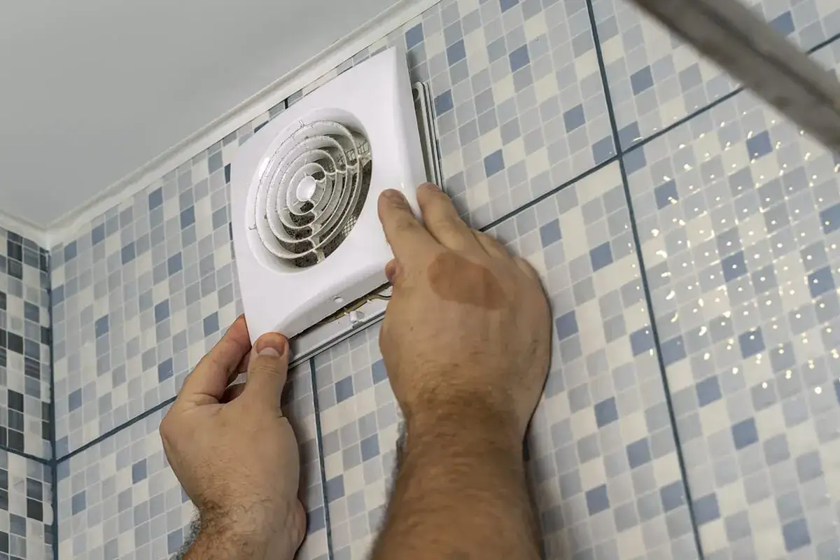 Mains de personne installant un ventilateur, une étape clé pour une bonne installation VMC dans une salle de bain carrelée.