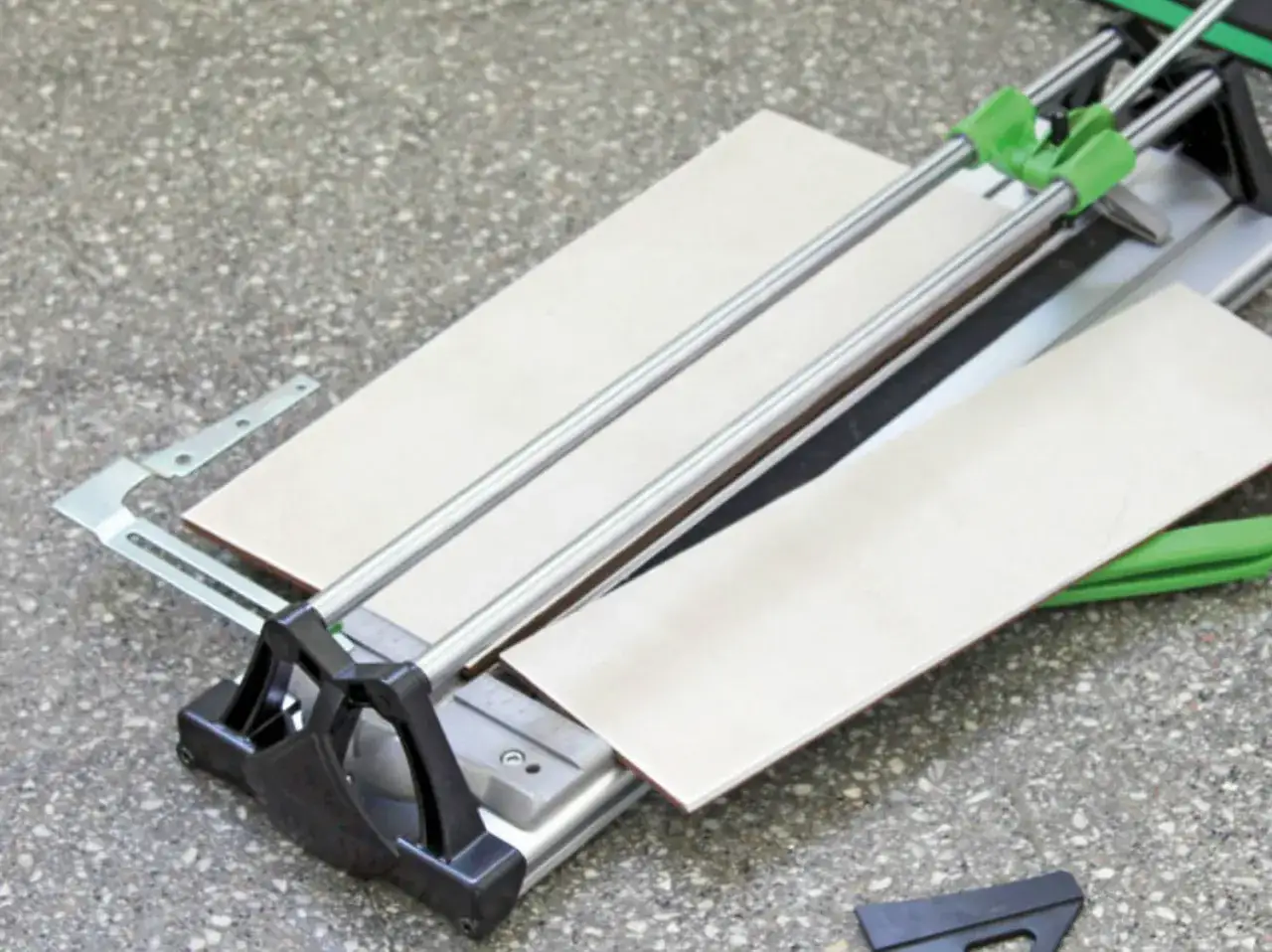 Machine de découpe de carrelage avec deux carreaux prêts à être coupés. L'outil est posé sur un sol en béton.