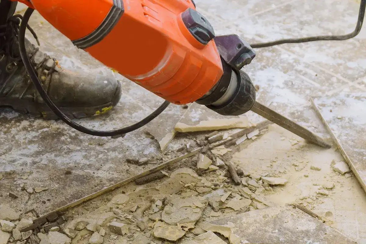 Marteau-piqueur orange en action pour enlever colle carrelage. Débris et poussière volent.