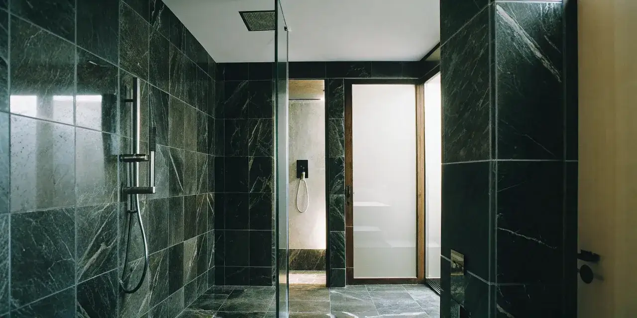 Salle de bain moderne avec murs et sol en grès cérame sombre veiné, douche vitrée et porte opaque.