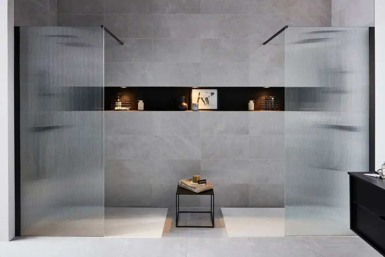Une grande salle de bain moderne avec deux douches vitrées aux portes texturées. Une niche murale noire abrite des articles de toilette et une décoration.