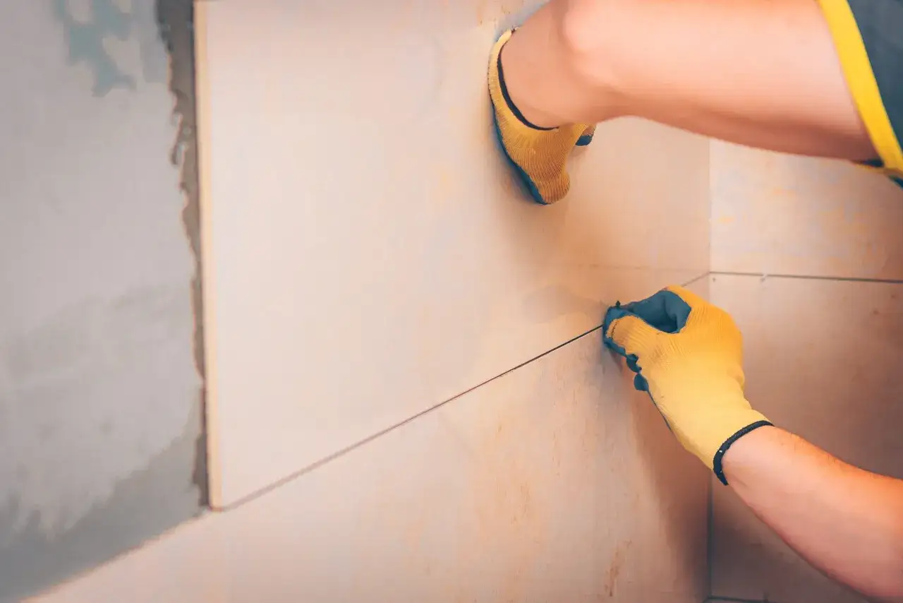 Mains gantées ajustant un joint carrelage sur un mur en cours de pose.
