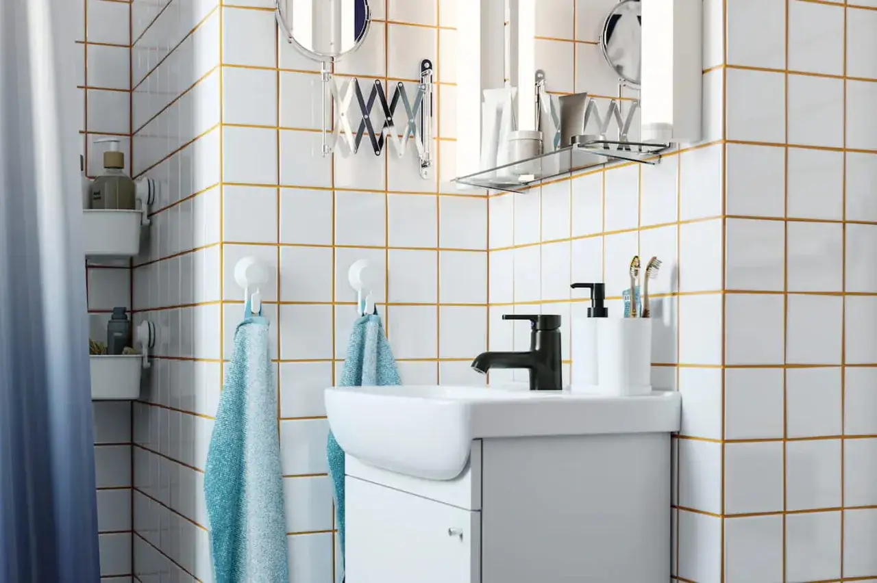 Salle de bain moderne avec carrelage blanc joint gris, lavabo, robinetterie noire et accessoires pratiques.