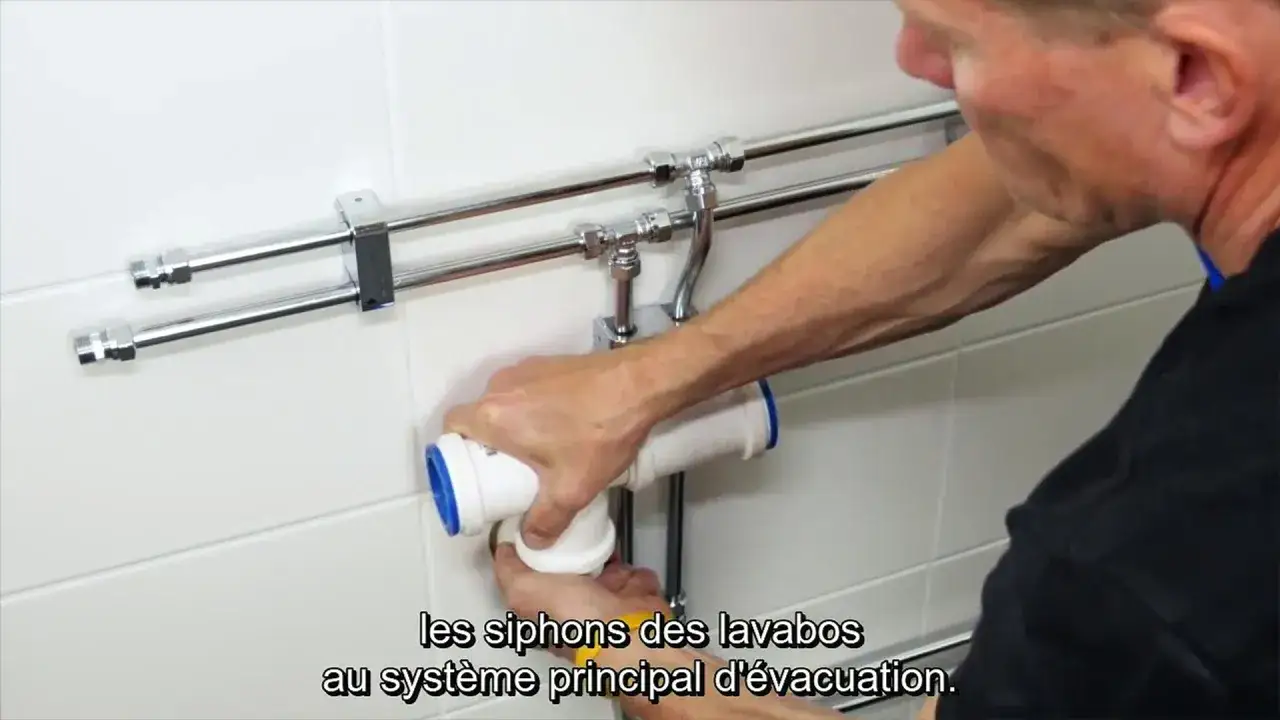 Installation des siphons pour l'arrivée d'eau double vasque. Un homme assemble les tuyaux d'évacuation.