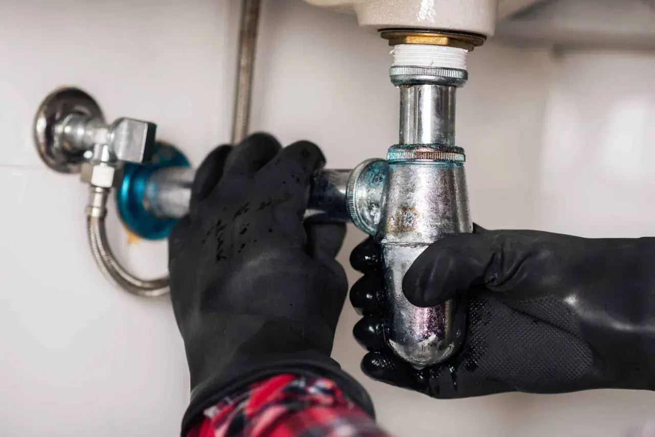 Mains gantées pour déboucher lavabo, démontant le siphon entartré.