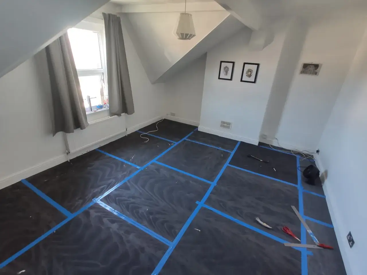 Préparation pour l'isolation phonique sur carrelage existant. Le sol est recouvert d'une bâche noire marquée de ruban bleu.