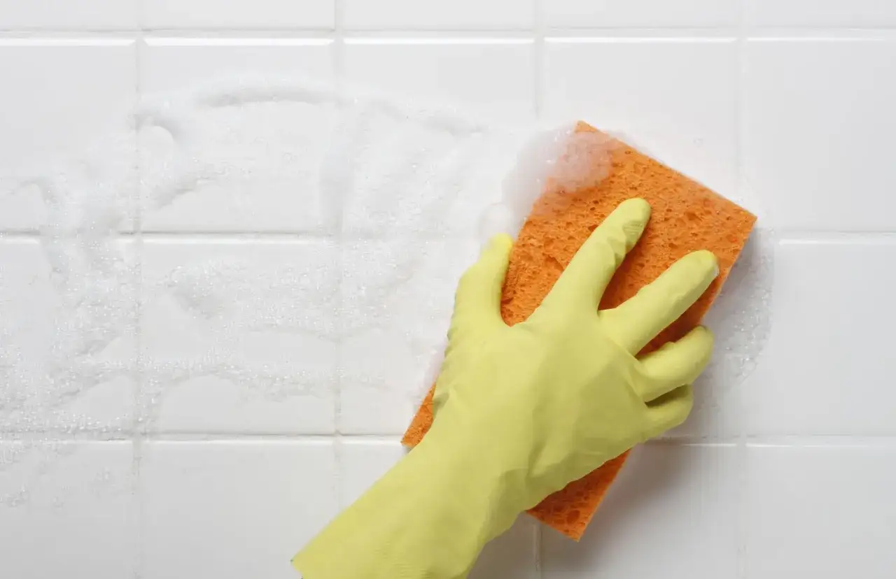 Main jaune frottant une tache sur carrelage qui ne part pas, avec de la mousse.
