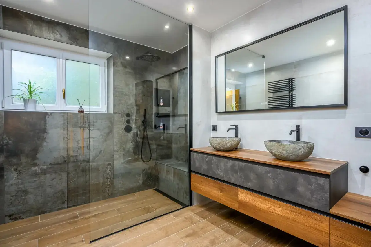 Salle de bain moderne avec douche en verre, double vasque en pierre naturelle et meubles en bois et béton ciré. Une vision de la tendance salle de bain 2026.