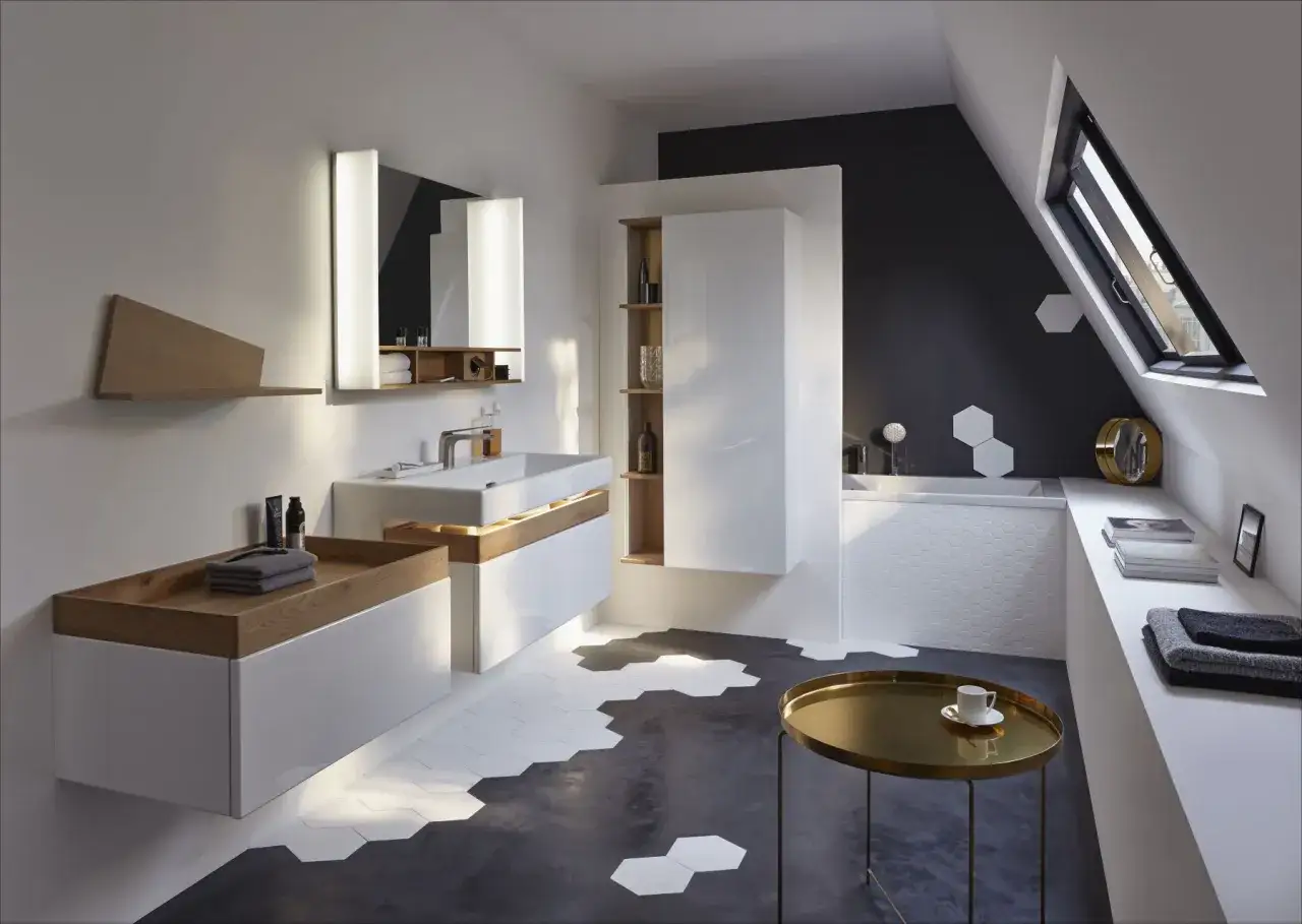 Élégante salle de bain sous pente avec vasque moderne, baignoire et rangements blancs laqués. Le sol hexagonal et la fenêtre de toit ajoutent du cachet.