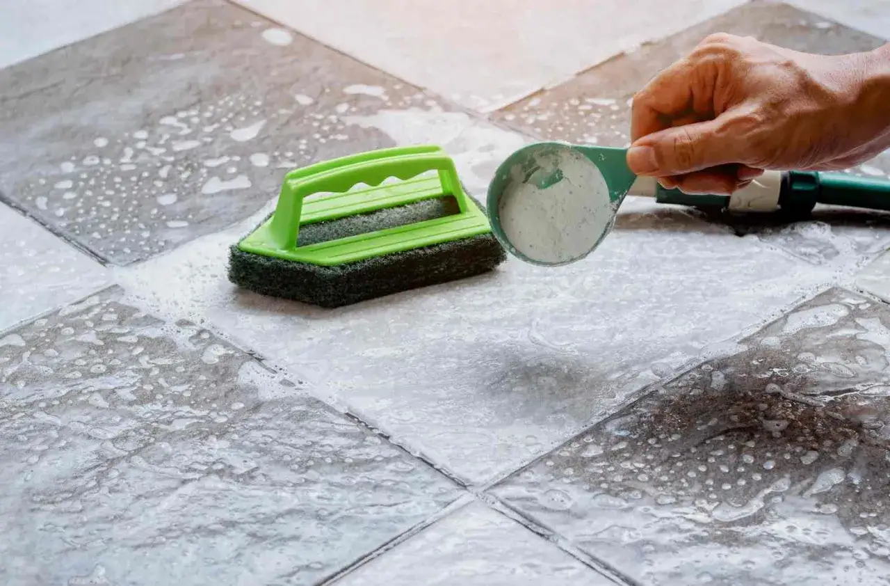 Maintenir un carrelage mat et poreux propre est facile avec ce produit. Une brosse verte et une cuillère de poudre nettoyante sont utilisées.