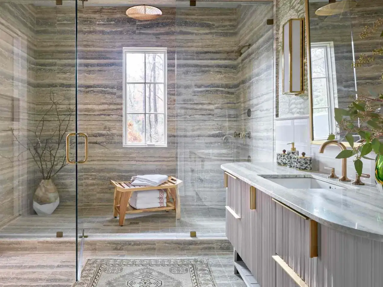 Salle de bain luxueuse avec un grand ressaut douche en marbre, un banc en bois et un lavabo &eacute;l&eacute;gant.