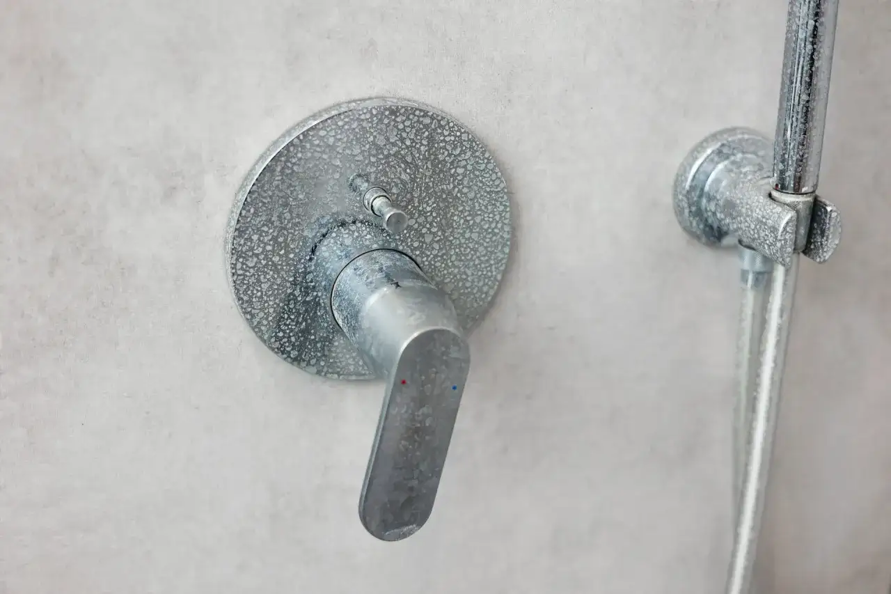 Robinet de douche avec traces de calcaire sur fond gris. Un détail qui rappelle l'importance de l'entretien dans une salle de bain.