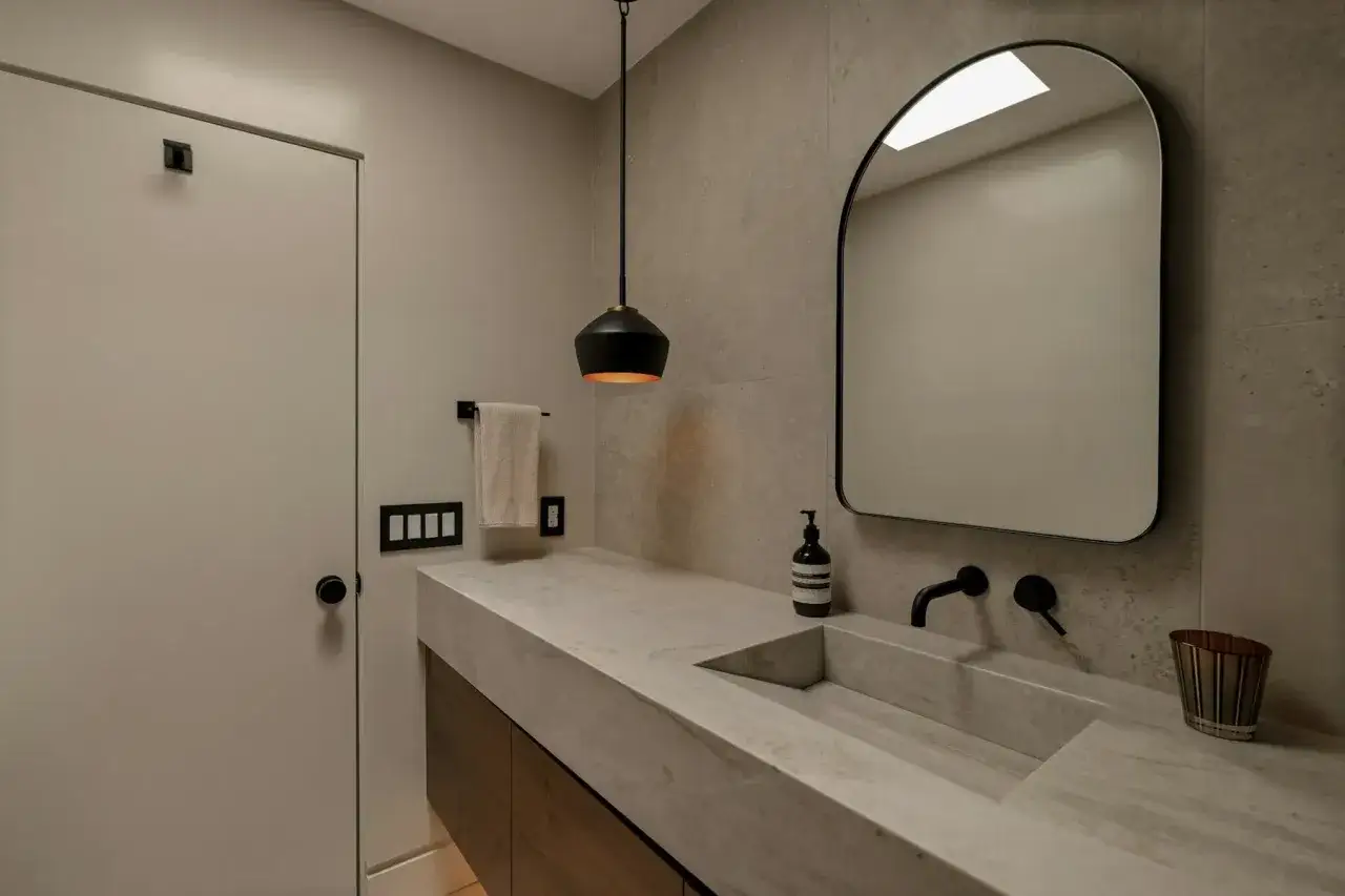 Plan vasque moderne en béton ciré ou résine, avec miroir arche, robinetterie noire et porte-serviettes.