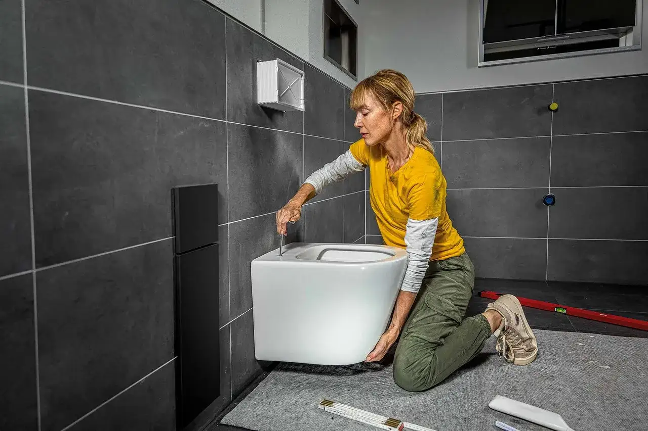 Une femme installe une nouvelle cuvette de WC suspendue. Le tarif remplacement wc complet est une prestation courante pour moderniser votre salle de bain.