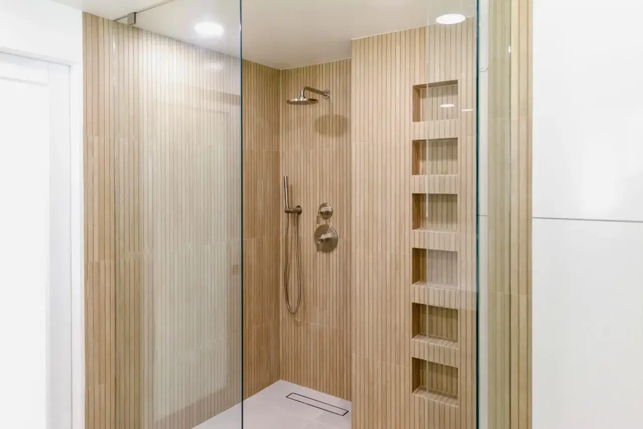 Douche moderne dans une salle de bain japandi, avec carrelage texturé en bois clair, niches intégrées et paroi en verre.