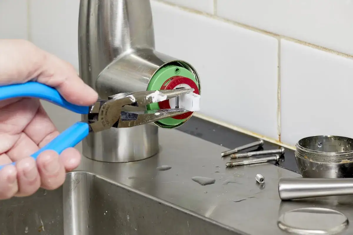 Maintenant, je comprends la durée de vie cartouche mitigeur. Une main utilise une pince pour retirer une pièce blanche d'un robinet.