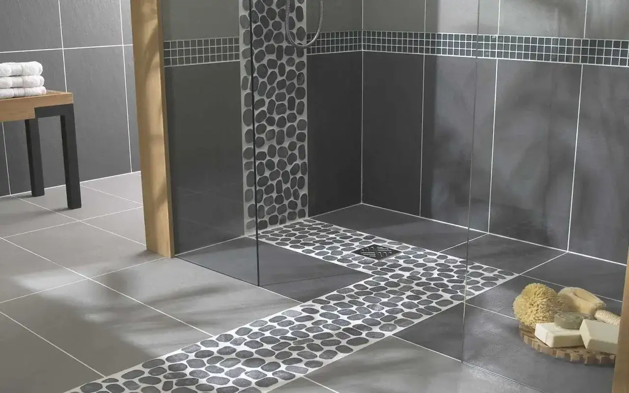 Carrelage moderne avec galets sur le receveur de douche, créant un chemin naturel vers la paroi vitrée.
