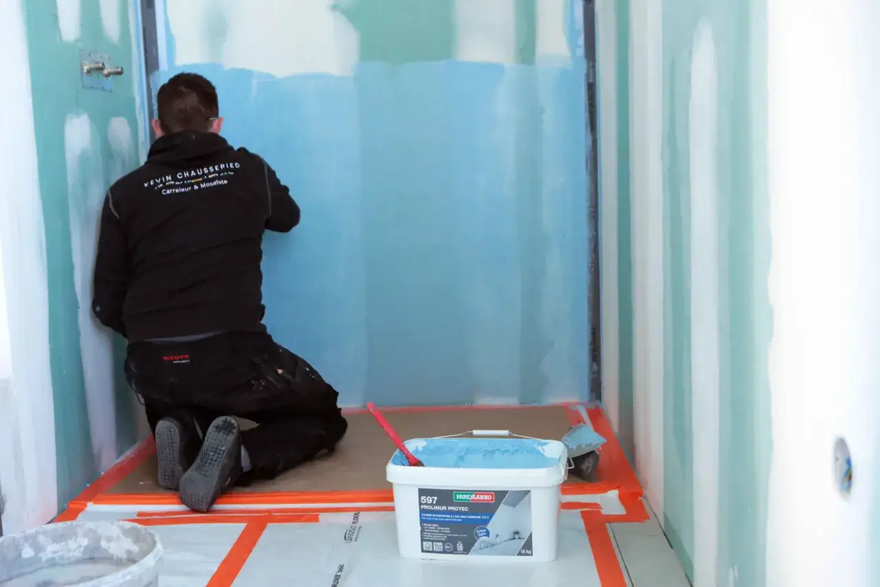 Un carreleur applique une protection étanche sur les murs d'une douche. Faut-il carreler toute la salle de bain ? Ce professionnel prépare le chantier.