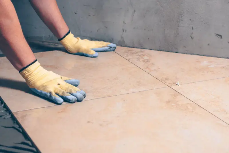 Pose de carrelage : mains gantées ajustant une nouvelle dalle sur la sous couche carrelage.