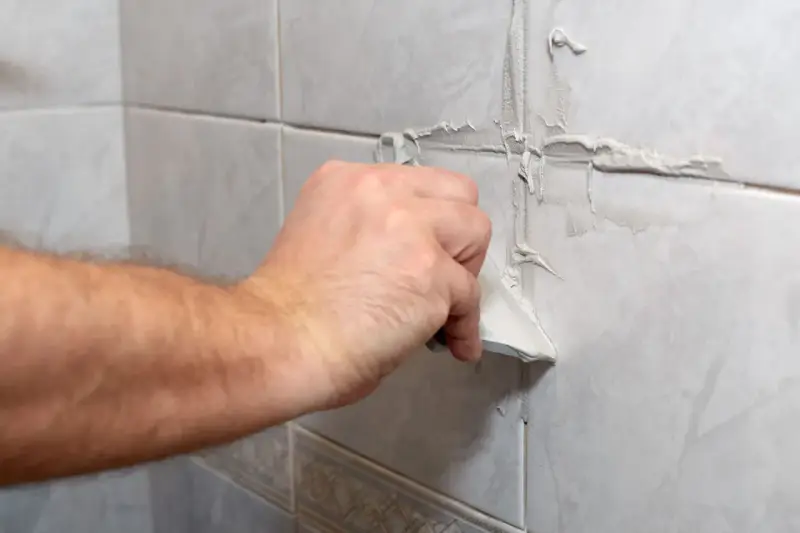 Main d'une personne appliquant du mastic sur les joints d'une salle de bain.